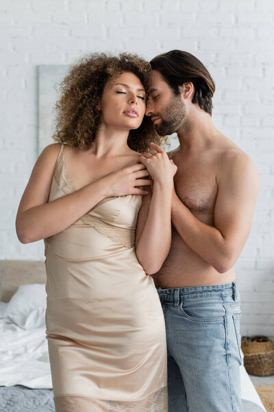 bearded and shirtless man seducing sexy woman in silk night dress standing with closed eyes 