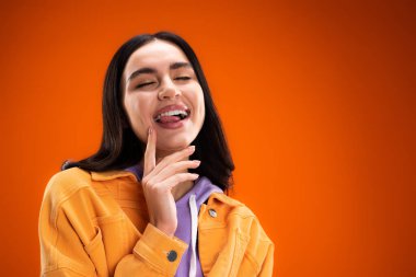 Young brunette woman sticking out tongue isolated on orange