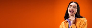 Young brunette woman sticking out tongue isolated on orange, banner 