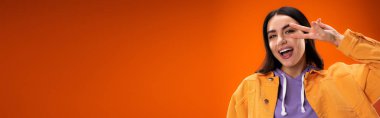 Positive young woman showing victory sign isolated on orange, banner 