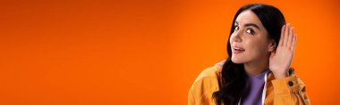 Smiling brunette woman listening isolated on orange, banner 