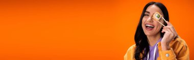 Young woman holding chopsticks and tasty sushi near face isolated on orange, banner 