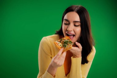 pretty brunette woman eating tasty pizza isolated on green
