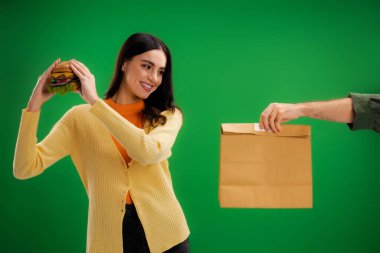 man holding food package near smiling woman with delicious burger isolated on green