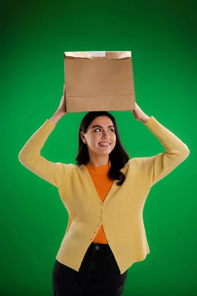 Stock image cheerful young woman holding paper bag above head isolated on green