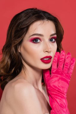 portrait of young woman with trendy magenta color eye shadow looking at camera isolated on pink 
