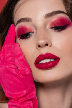 close up of young woman with magenta color glove touching face