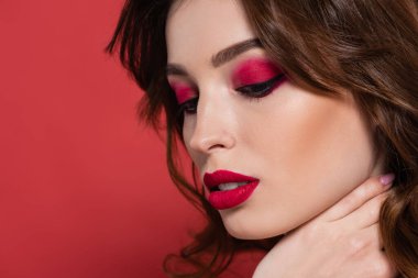young woman with magenta color makeup touching neck isolated on pink 