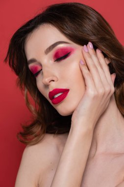 portrait of young woman with magenta color eye shadow gently touching face isolated on pink 