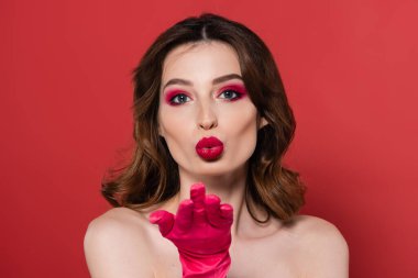 portrait of young woman with magenta color eye makeup sending air kiss isolated on pink 
