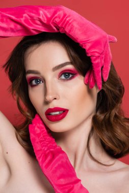 portrait of young woman with magenta color eye makeup and gloves posing isolated on pink 