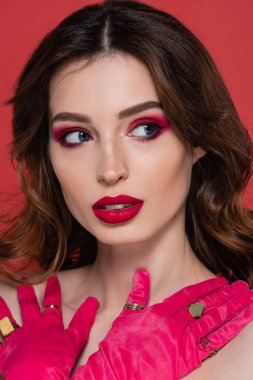 portrait of woman with magenta color gloves and golden rings posing with crossed arms isolated on pink