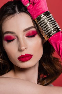 portrait of young woman in magenta color glove with golden ring and bracelet posing  with closed eyes isolated on pink 