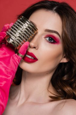 portrait of young woman in magenta color glove holding golden bracelet isolated on pink 