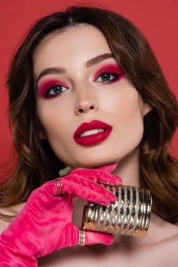 portrait of young woman in magenta color glove with rings holding golden bracelet isolated on pink 