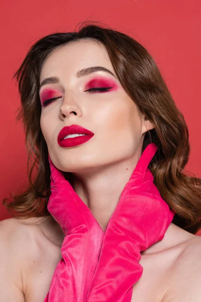 portrait of young woman with magenta color eye shadow touching neck isolated on pink