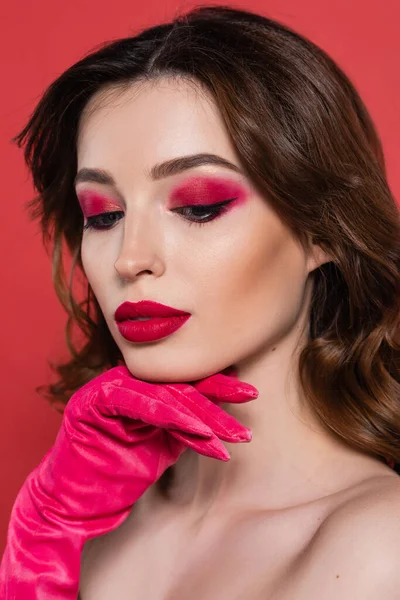 portrait of pretty young woman with magenta color eye shadow posing isolated on pink 