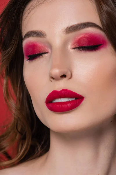 close up of young woman with closed eyes and magenta color eye shadow isolated on pink
