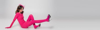 full length of happy young woman in hat and magenta color dress having fun on grey background, banner 