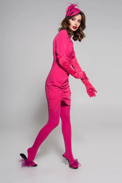 Stock image full length of young woman in magenta color dress and shoes with feather posing on grey 