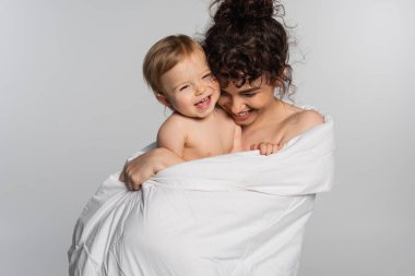 cheerful mother and toddler baby girl covered in duvet isolated on grey 