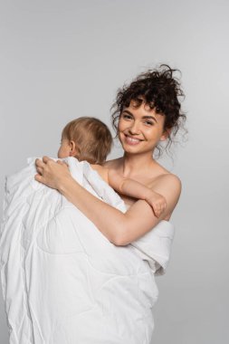positive mother and toddler baby girl covered in duvet isolated on grey 