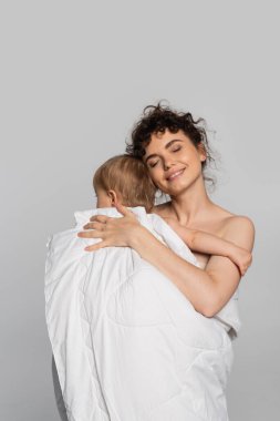 happy mother with closed eyes and toddler baby girl covered in duvet isolated on grey 