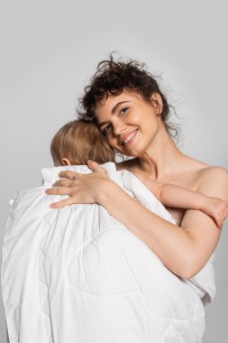 happy mother hugging toddler baby girl covered in duvet isolated on grey 