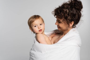 pleased mother and toddler baby girl covered in duvet isolated on grey 