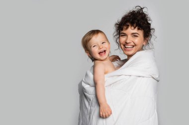 happy mother and positive toddler daughter covered in duvet isolated on grey 