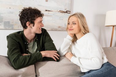 young woman with blonde hair looking at curly boyfriend in living room 