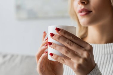 cropped view of young woman in white sweater holding cup of coffee 