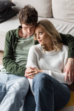 high angle view of young man with curly hair hugging sensual blonde woman in living room 