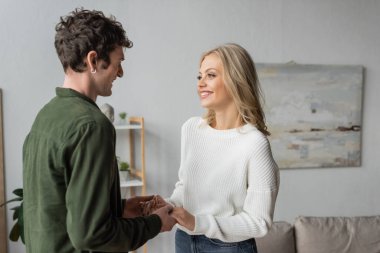 happy blonde woman in white sweater holding hands with curly man in shirt 