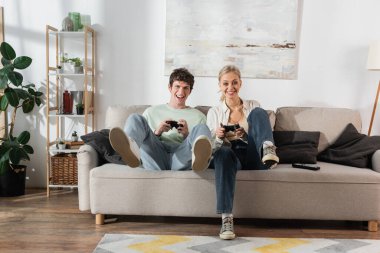 KYIV, UKRAINE - OCTOBER 24, 2022: excited young couple holding joysticks while playing video game