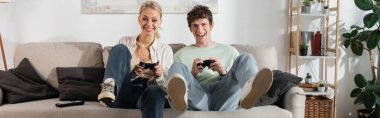 KYIV, UKRAINE - OCTOBER 24, 2022: excited young couple holding joysticks while playing video game, banner 