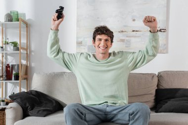 KYIV, UKRAINE - OCTOBER 24, 2022: excited young man in sweatshirt holding joystick in living room 