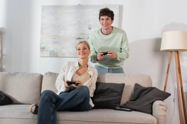 KYIV, UKRAINE - OCTOBER 24, 2022: joyful young couple holding joysticks while playing video game in living room 
