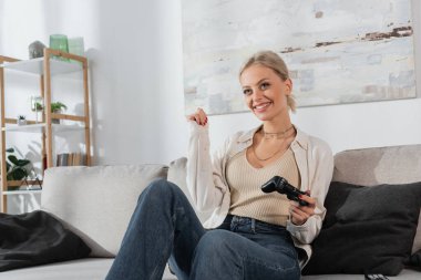 KYIV, UKRAINE - OCTOBER 24, 2022: joyful young woman holding joystick while playing video game on couch 