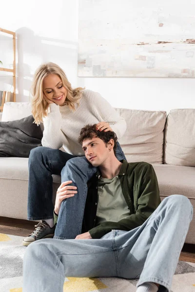 Curly Young Man Hugging Leg Happy Girlfriend Living Room — Stockfoto