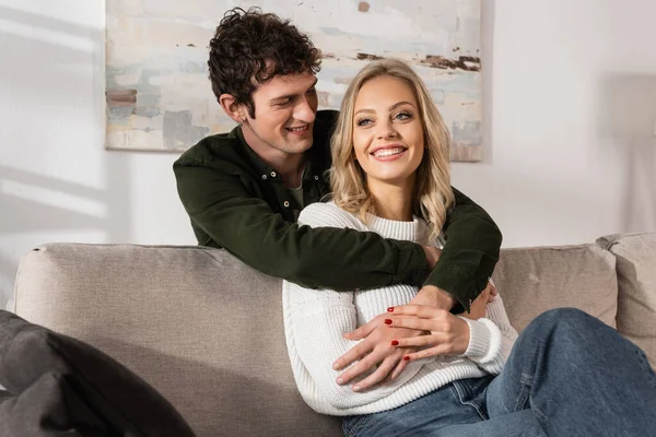 Curly Young Man Hugging Happy Blonde Woman Living Room — Stockfoto