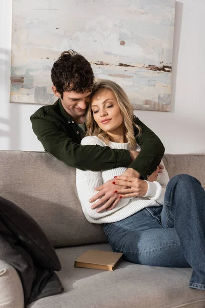 curly young man hugging pleased blonde woman in living room 