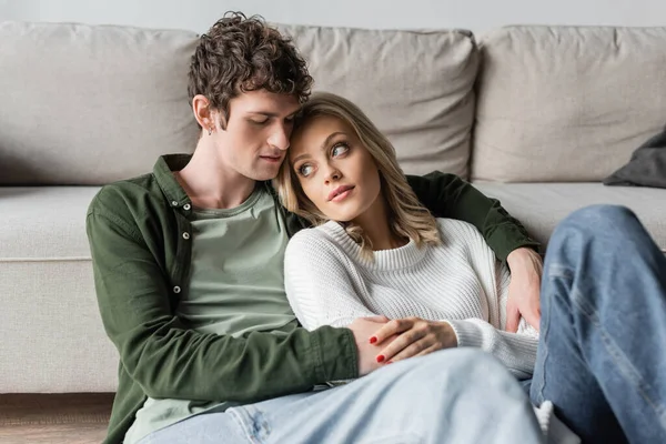 young man with curly hair hugging blonde woman near sofa in living room 