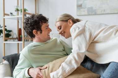 cheerful young couple laughing while having pillow fight in living room 