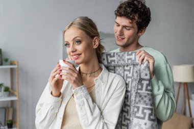 cheerful and caring man covering happy blonde woman with blanket 