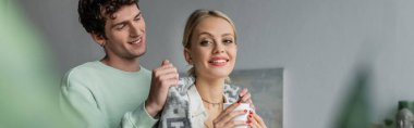 cheerful and caring man covering smiling blonde woman with blanket, banner 