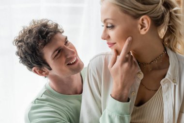 cheerful man in sweatshirt touching face of pretty and blonde girlfriend 