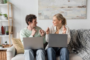 excited young bloggers rejoicing near laptops while sitting on couch 