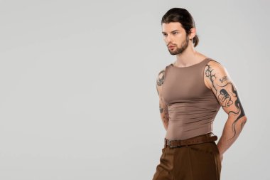 Long haired tattooed man looking away while standing isolated on grey 