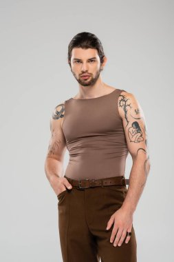 Stylish tattooed man in tank top posing isolated on grey  clipart